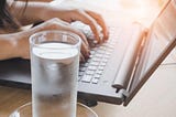 Frosty glass of water next to a person working on laptop