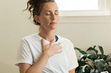 woman with hand over heart and on stomach in yoga clothes setting affirmations