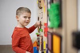 Young boy playing with a wall of sensory toys