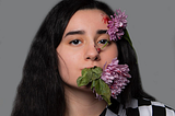 A woman with a large flower in her mouth, and one covering her forehead
