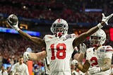 Ohio State wide receiver Marvin Harrison throws his two hands up in celebration, holding a football in his right hand.