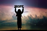 Silhouette of a woman holding a sign saying Hope before a sunrise