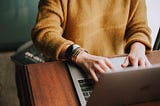 Close up of a person in a yellow sweater typing on a laptop keyboard