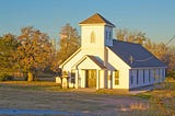 white church in a grassy clearing surrounded by trees