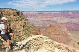 A man wearing a white hat sits on the edge of the Grand Canyon