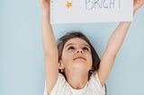 Little girl holding up a sign that says ‘Shine Bright’