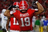 Brock Bowers of the University of Georgia football team flexes his muscles with the football in his right hand.