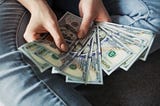 Reaching 8 figures: Someone holding 100 U.S. dollar banknotes