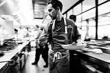 Restaurant photography of chef rushing in kitchen, photographed industrial style in black and white.