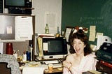 Bitsy as a young software engineer, circa 1984, with vending machine coffee and a pack of Lorna Doone cookies, goofing around in her office at IBM with a microfiche and a stuffed moose on her head.