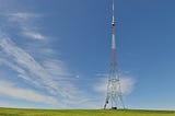 Image of a telecommunication mast in a green field with blue cloudy sky