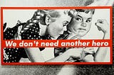 Barbara Kruger’s large black and white illustration of two kids in 5’s advertising style looking a their arm muscles — with red text banner splashed across reading: We don’t need another hero.