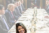 Lindsey Galligan popping up in front of a table full of men and whatever Trump is called these days.