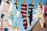 A row of odd socks hung on a washing line. The sky in the background is blue with white flufy clouds