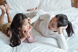 Mother and young daughter laying on bed talking