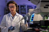 NIST biomedical engineer Laurie Locascio wears safety glasses and a lab coat as she places a water sample on a chip.