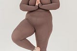 A woman in brown yoga clothing in Tree Pose.