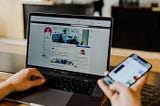 A person looking at two different social media networks on a laptop and mobile phone simultaneously.