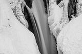 A black and white Pacific Northwest nature photograph of a snow covered, partially frozen Christine Falls at Mount Rainier National Park, Washington.