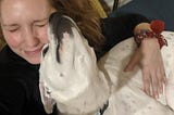 Laura, in a black sweatshirt, cuddling her white and black dog, Ivy.