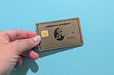 The American Express® Gold Card being held up in front of a bright blue wall