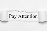 Image of words “Pay Attention” revealed behind torn pieces of paper.