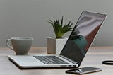 silver laptop and white cup on table — you don’t need an ‘all signing and dancing’ laptop to start your business.
