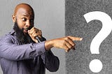 jclay pointing holding a microphone with a question mark