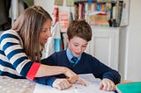 a woman pointing to something on a notebook, teaching a male young student