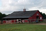 Red barn with horse inside fence.