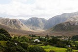 A lush green Irish valley with trees and houses, surrounded by brown treeless mountains