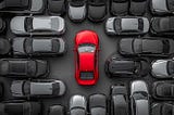 Red car stands out among grey vehicles at a salvage auto auction, highlighting variety and opportunity.