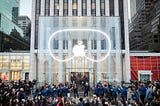 Apple Vision Pro event in NYC Apple store, showing clear glass building with apple logo and shape of the googles behind it.