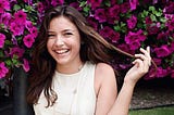 Young woman with long brown hair smiles and twirls a piece of long hair