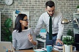 One person interrupts another at her desk