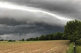 A storm rolls in across an Illinois field. The clouds are looming, gray and ominous, but in the middle there is a streak of lighter sky, like hope.