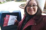 Lyndsey with a mailbox holding two stamped absentee ballots. Her expression is a cross between excitement and apprehension.