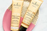 Pale yellow tubes of Sukin Reef Safe Sheer Touch SPF30 Sunscreen in Untinted and Light/Medium on a pink and gold plate