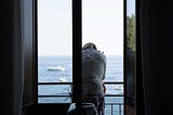 A woman standing on the balcony looks out at the ocean.