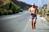 A runner in a pair of shorts running beside a long straight road