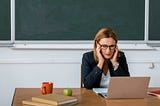 Teacher working at computer, head in hands.