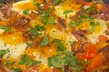 Delicious protein in my homemade shakshuka. Sunnyside eggs on bed of onions tomatoes, spices, and garnished with fresh cilantro