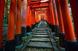 Steep stone stairs flanked by rows of vibrant vermillion torii gates leading up the forested slopes of Fushimi Inari Taisha in Kyoto, Japan.