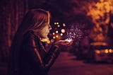 A woman blows magical dust from her hands on a city street.