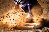 A baseball player sliding into a base with dirt everywhere.