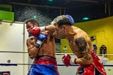 Two men fighting in a boxing ring with one wearing a red shirt.