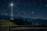 starry dark night across a meadow with a bright light shining down on a home