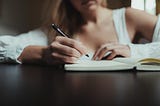 Woman sitting down, writing in a notebook with a pen