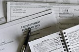 Tax documents and 1099 forms with a tax statement, pen and business log on a desk during tax season. Photo by Olga DeLawrence on Unsplash