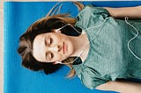 Tranquil woman resting on yoga mat in earphones at home